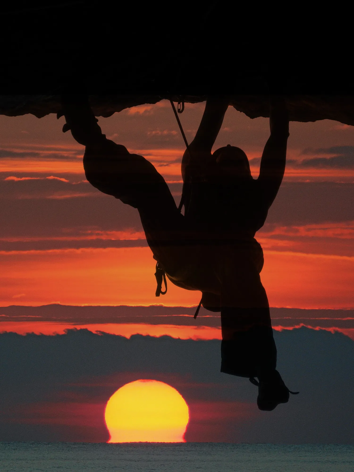 Uno scalatore appeso a uno strapiombo, in controluce sul tramonto