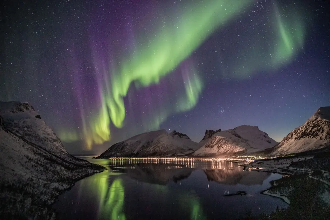 Aurora boreale verde sopra montagne innevate e un lago