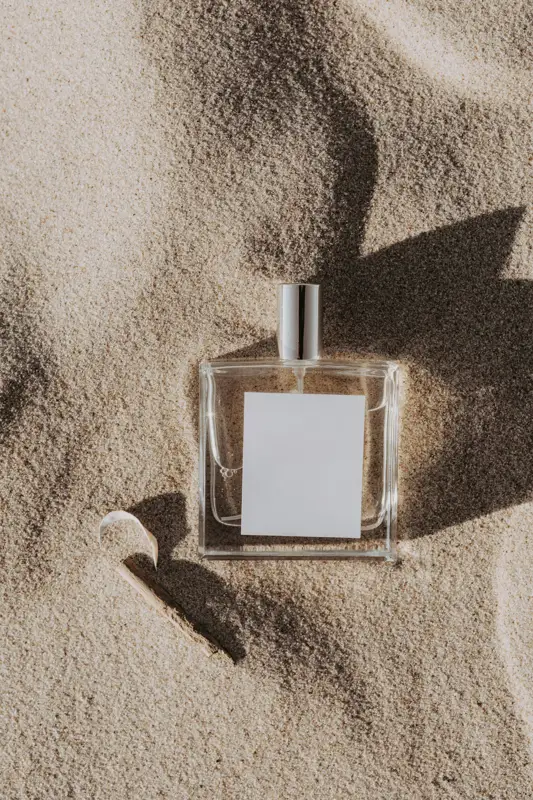Flacone di profumo con etichetta bianca sulla sabbia